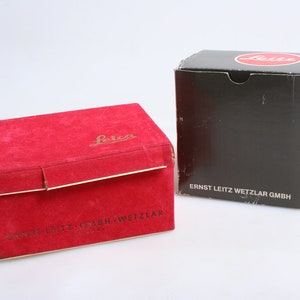 Puede incluir: Dos cajas de terciopelo rojo con el logotipo de Leica y el texto "Ernst Leitz GmbH Wetzlar" en la parte inferior. La caja de la derecha es negra con el logotipo de Leica y el texto "Ernst Leitz Wetzlar GmbH" en la parte inferior.