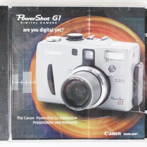 以下が含まれることがあります： Canon PowerShot G1デジタルカメラのソフトウェアCDケース。カバーにはシルバーのカメラが写っています。テキストには「PowerShot G1 DIGITAL CAMERA」、「are you digital yet?」、「3.3 MEGA PIXELS」、「The Canon PowerShot G1 Interactive Presentation and Resource」と記載されています。