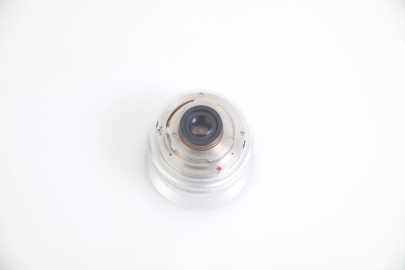 Pu&ograve; includere: Un obiettivo per fotocamera trasparente e circolare con un centro nero e componenti metallici argentati. L'obiettivo ha una copertura in plastica trasparente e scanalata ed &egrave; posto su uno sfondo bianco. Accessorio fotografico.