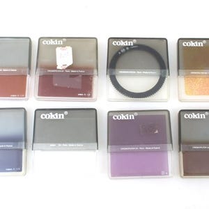 Könnte beinhalten: Acht graue Plastikbehälter mit dem Wort "cokin" auf der Vorderseite. Jeder Behälter enthält einen Filter in einer anderen Farbe.