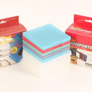 Peut inclure: Une pile de boîtiers de disquettes 3,5" colorés en bleu, rouge et violet, à côté de deux boîtes rouges avec l'inscription "3.5" Dual Disk Cases" et "Disk Transporters". Les boîtes ont un trou de suspension et le texte "Organize" et "Innovative".