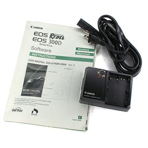 May include: A Canon EOS Rebel EOS 300D Digital camera software instruction manual, battery charger, and power cord. The manual is white with black and green text. The charger is black.
