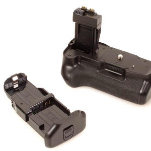 Könnte beinhalten: Schwarzer Kamerabatteriegriff mit strukturierter Oberfläche und separatem Batteriefach. Der Griff hat einen oberen Anschluss und ein Steuerrad. Das Batteriefach ist abgenommen und hat einen Riegel.