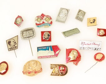 Op de afbeelding: Een verzameling vintage emaille-speldjes met portretten van Vladimir Lenin, het Kremlin en andere Sovjet-symbolen. De speldjes zijn in verschillende kleuren, waaronder rood, goud en zilver.