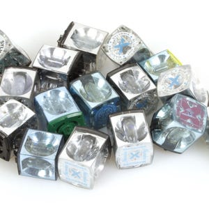 May include: A collection of vintage Sylvania Magicube flash cubes. The cubes are clear with silver reflectors and black bases. Some cubes have blue, green, or purple accents and logos.