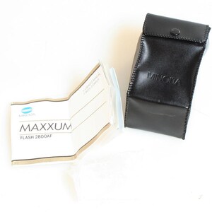 May include: A black leather case with the word "MINOLTA" embossed on it.  A white and blue instruction booklet for a Minolta Maxxum Flash 2800AF is also pictured.