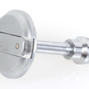 Könnte beinhalten: Ein glänzendes, silberfarbenes Metallwerkzeug mit einem kreisförmigen Kopf und einem langen, schlanken Griff. Der Kopf hat einen klappbaren Abschnitt und ein kleines, kreisförmiges Detail. Der Griff endet in einem konischen, gekerbten Design.