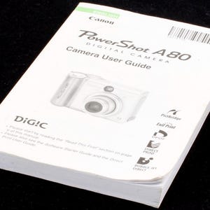 May include: A white Canon PowerShot A80 digital camera user guide with the camera pictured on the front cover. The guide includes information about PictBridge, Exit Print, EPOF, Direct Print, and Bubble Jet Direct.
