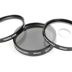 May include: Three black camera lens filters with white text. The filters are labelled "Foggilizer", "Quantaray CPL", and "Quantaray Spot". Each filter has a 52mm diameter.