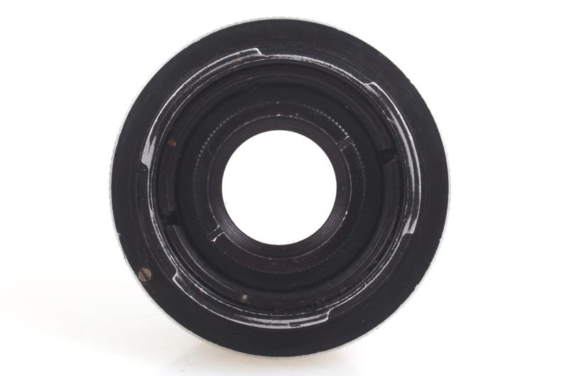 May include: A close-up shot of a black and silver camera lens adapter. The adapter has a circular design with a central opening and a series of concentric rings. The outer ring is silver, while the inner parts are black.