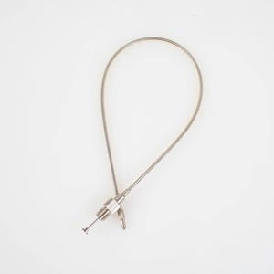 May include: A silver-colored, flexible cable with a loop, attached to a small, metallic component with a pin and a small ring. The cable is positioned against a white background.
