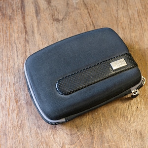 Puede incluir: Una funda negra con cremallera, un tirador de cremallera gris y un parche de cuero negro con el texto "GRAB & GO" en blanco.