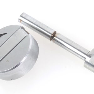 Puede incluir: Un componente metálico plateado con una base redonda y una flecha direccional. También hay otra pieza metálica a juego con un extremo en forma de horquilla. Los artículos parecen ser piezas de máquina.