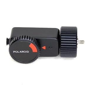 Op de afbeelding: Zwart Polaroid camera-accessoire met een ronde wijzerplaat met de merknaam en een rode accentkleur. Het accessoire heeft een rechthoekige behuizing en een cilindrisch onderdeel met ribbels. Een kleine schroef is zichtbaar.