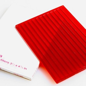 May include: A red safelight filter for photography, labeled "Ultima Safelight filters 3 1/2 x 4 1/4 in Orange" and "EPOI No. 31 029".