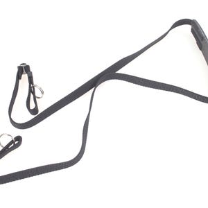 Puede incluir: Una correa de cámara negra con un reposacabezas acolchado y correas ajustables. La correa tiene anillos metálicos para la fijación y está diseñada para llevarse alrededor del cuello. La correa está hecha de un material tejido duradero.