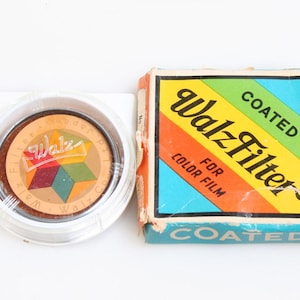 May include: Vintage camera filter and box. The filter is in a clear plastic case. The box is rectangular with a colorful design and the words "Walz Filter" and "Coated" printed on it. The box is for color film.