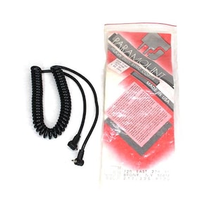 Könnte beinhalten: Ein schwarzes Spiralsynchronisationskabel mit zwei geraden Kabeln und Steckern. Das Kabel befindet sich neben einer Plastikverpackung mit dem Text "PARAMOUNT HEAVY DUTY SYNC CORDS" und "MADE IN USA".