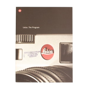 May include: A brown and white book cover with the text "Leica. The Program" and a close-up image of a silver camera lens with a red circle logo that says "Leica".