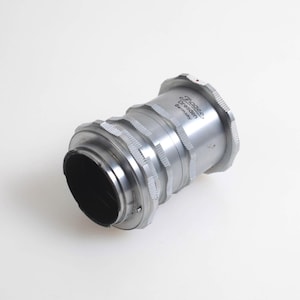 Può includere: Un obiettivo per fotocamera color argento con interno nero. L'obiettivo ha un design a coste e il testo "Rodagon Dresden Germany". L'obiettivo è su sfondo bianco.