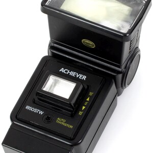 May include: Black flash unit with a white flash bulb. The flash unit has a label that reads "ACHIEVER" and "1850STW". It also has a dial with markings for 1/10, 1/1, and 1/10. The flash unit has a label that reads "AUTO THYRISTOR".