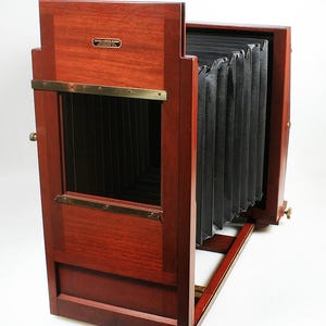 May include: A classic wooden camera with a bellows design and brass detailing. The camera has a dark wood finish. The text "FOLMER & SCHWING DIVISION EASTMAN KODAK CO. ROCHESTER, N. Y." is on a metal plate.