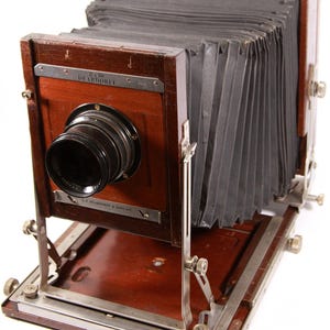May include: A vintage 8x10 Deardorff view camera with a bellows and a lens. The camera is made of wood and has a metal base.