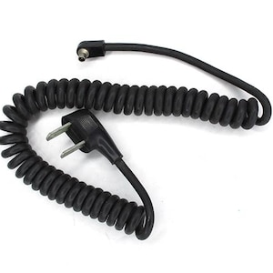Puede incluir: Un cable de alimentación negro en espiral con un enchufe de dos clavijas y un conector. El cable está hecho de un material flexible similar al caucho. El fondo es blanco.