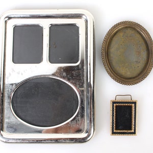 May include: Three silver and gold picture frames with black velvet backing. The largest frame has three openings, two rectangular and one oval. The other two frames are smaller, one round and one rectangular.