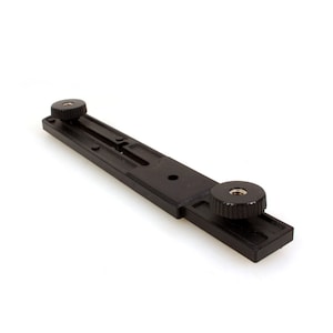 Puede incluir: Accesorio de cámara de plástico negro con dos botones ajustables y una ranura central. El accesorio está diseñado para montarse en una cámara u otro equipo.