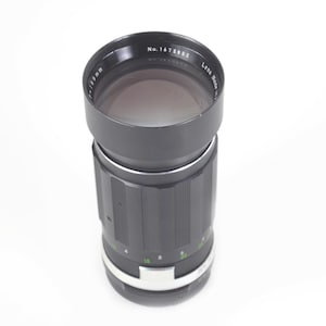 May include: A black camera lens with a silver accent ring. The lens has a black hood and a series of numbers and markings. The text "No. 1472682" is visible on the lens hood. The lens is cylindrical in shape.