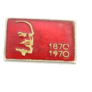 May include: Red enamel pin with a gold outline featuring a profile of a man's face and the years "1870 1970".