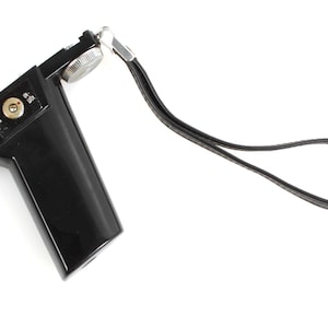 May include: A black camera grip with a silver dial and a black wrist strap. The grip has a rectangular shape with a rounded handle. The dial is silver and has a textured surface. The wrist strap is made of black leather.