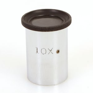 Puede incluir: Una lupa de color plateado con un borde de goma negro y una magnificación de 10x.