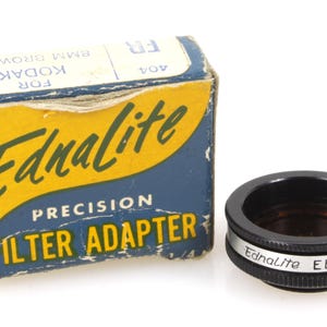 May include: A blue and yellow box with the text "Ednalite Precision Filter Adapter" for Kodak Brownie 8mm. A black filter adapter with the text "Ednalite EB USA" is next to the box.