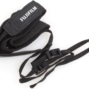May include: Black camera strap with a black leather pad that says "FUJIFILM" in white lettering. The strap has two black plastic clips.