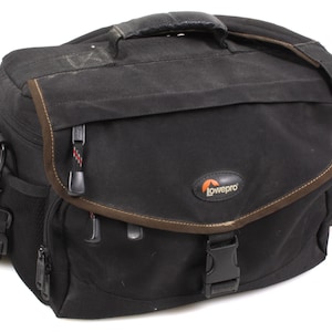 May include: Black Lowepro camera bag with a brown trim and handle. The bag has a shoulder strap, multiple compartments, and a buckle closure. The Lowepro logo is visible on the front.