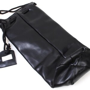 May include: A black leather drawstring bag with a rectangular tag. The bag is made of a smooth, shiny material and has a drawstring closure. The tag is black with a white rectangle.