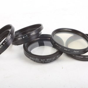 Könnte beinhalten: Vier schwarze Objektivfilterringe mit dem aufgedruckten Text "SER 6-7" und "JAPAN". Ein Filterring hat den aufgedruckten Text "SPIRATONE 6-7 STEP-UP USA". Ein weiterer Filterring hat den aufgedruckten Text "That Stellar Ser.7 Japan". Der letzte Filterring hat den aufgedruckten Text "Grostar 180 Ser.7".