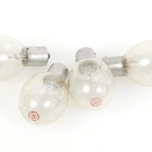 Pode incluir: Quatro lâmpadas vintage com um bulbo de vidro transparente e fosco e uma base prateada. Cada lâmpada tem um logotipo GE vermelho. As lâmpadas estão dispostas sobre um fundo branco.