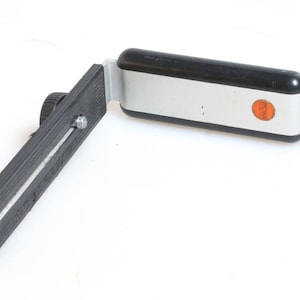 May include: A black and silver camera bracket with a knob on the side. The bracket is designed to attach to a camera and allow for a flash to be mounted at a 90-degree angle.