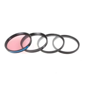 May include: Four camera lens filters, one with a pink coloured glass and three clear glass filters.