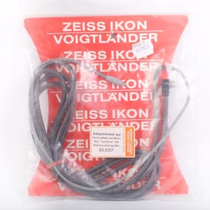 May include: A gray adapter cable for use with Mavi-flex "synchron" with electronic flash units. The cable is packaged in a clear plastic bag with a red and white printed label that reads "ZEISS IKON VOIGTLANDER".