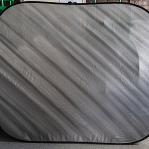 Op de afbeelding: Een grijze stoffen achtergrond met een zwarte rand. De stof heeft een diagonaal patroon en is licht gekreukt.