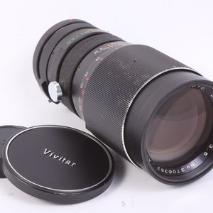 May include: A black Vivitar 200mm f/3.9 lens with a silver ring and a black lens cap. The lens has a black and silver lens cap with the Vivitar logo.