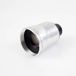 May include: A silver lens with the text "WAIFLEX SUPER-BRIGHT" is displayed against a white background. The lens has a black end and a ridged, cylindrical body. The lens is designed for photography.