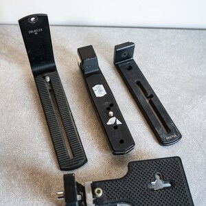 Puede incluir: Cuatro placas de trípode de cámara negras. Una placa tiene el texto "GRAFLEX". Otra placa tiene el texto "VIVITAR".