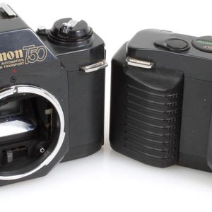 May include: Two black Canon T50 film cameras are displayed side-by-side. The cameras have a silver lens mount and a flash mount on top. The Canon logo and model number are printed in gold. The cameras are on a white background.