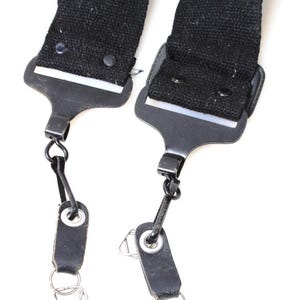 May include: Close-up of two black suspenders with metal clasps and leather loops. The suspenders are made of a sturdy black fabric and feature metal hardware for attachment. The leather loops have metal rings.