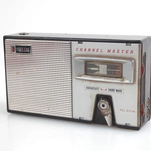 Può includere: Radio Channel Master vintage con griglia altoparlante argentata e pannello di controllo argento e nero. Il testo "CHANNEL MASTER" è in rosso e "TRDELUXE" sull'altoparlante. Con controllo del volume e quadrante di sintonizzazione.